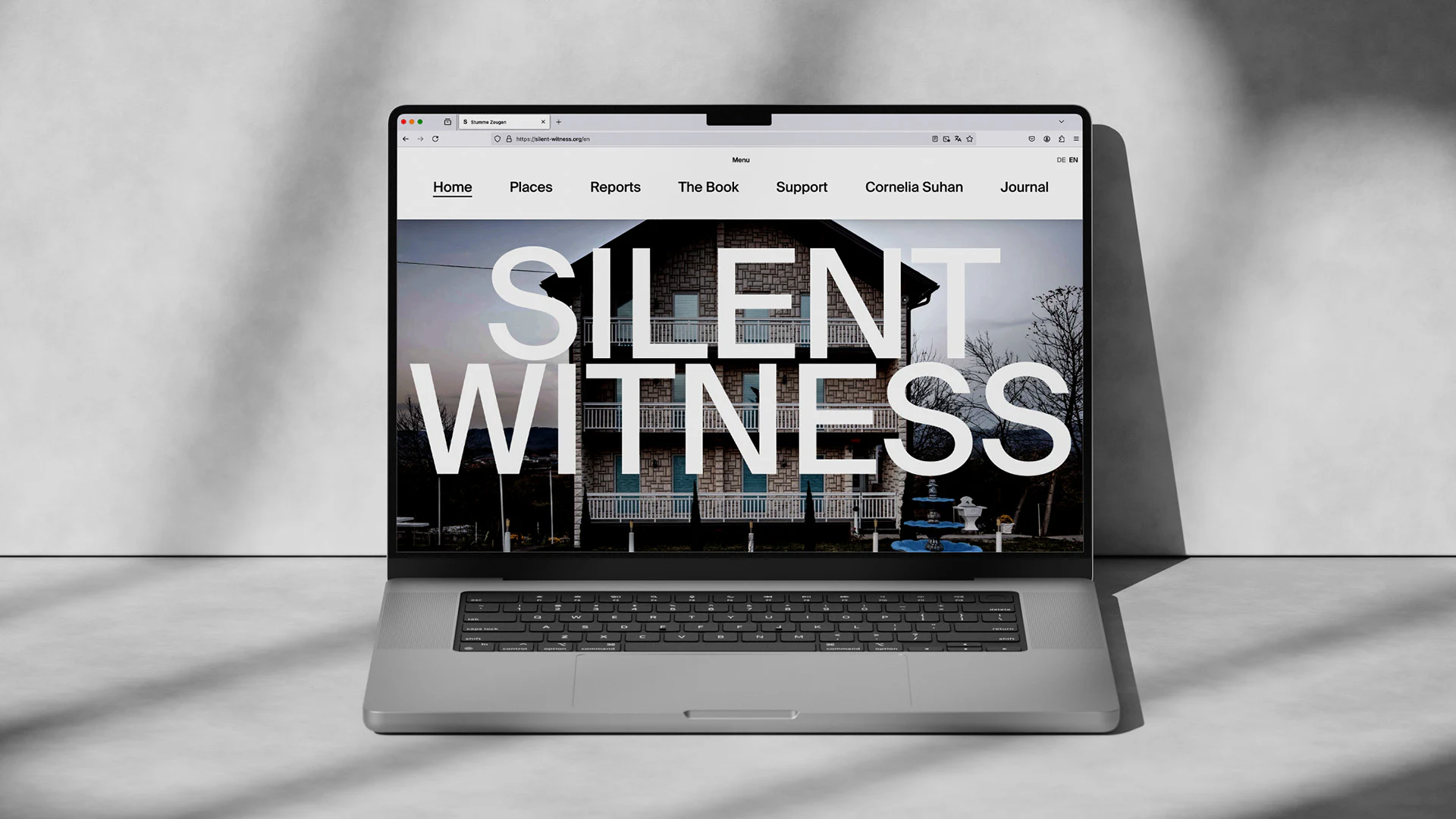 Silent Witness桌面首页的两行白色大标题覆盖建筑照片，上方浅色条排列导航和DE EN语言项