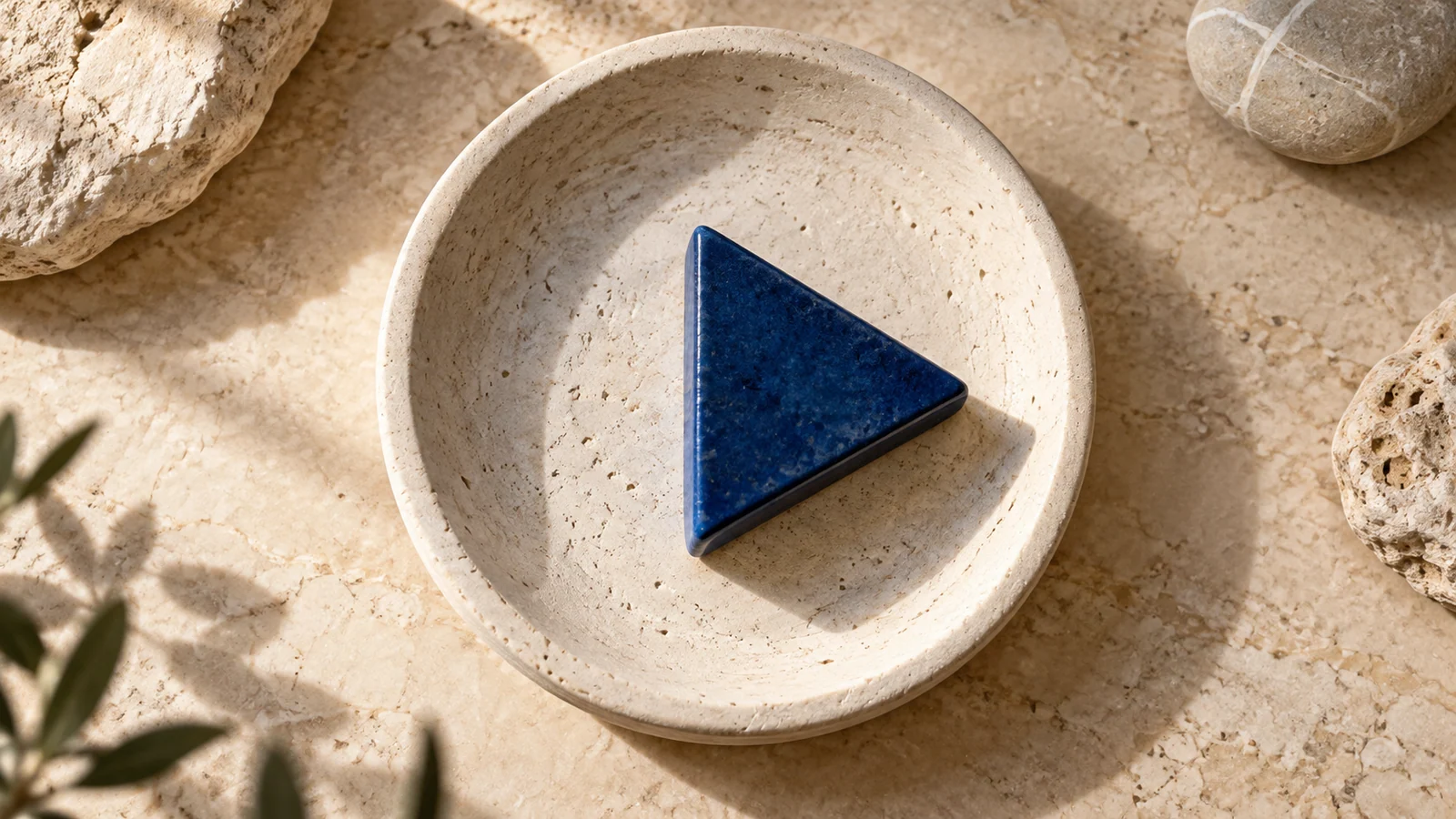 A triangular ceramic object inside a circular stone dish illustrates the visual weight of a play icon